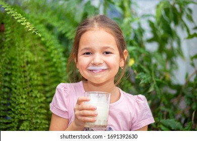 The girl drank kefir or milk from a glass and licks her tongue with her lips. Kefir mustache