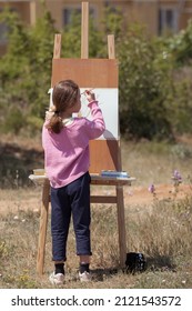 The Girl Draws In The Park On An Easel, Plein Air. Child Learns To Draw In Nature