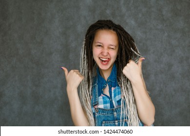 The Girl In The Dreadlocks Is Smiling. Smiling Girl On Gray Background. Portrait Of A Teenager With Dreadlocks. Banner For Advertising With A Girl. Teen Shows Ok