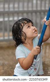 A Girl Drenched In The Rain Shows An Excited Facial Expression While Poking At Something With A Blue Stick. Little  Malaysian Girl