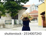 Girl in dress and hat against the background of architecture of the Old Town of Trebinje: Clock Tower, stone mosque and historic houses. Female tourist during a trip to Bosnia and Herzegovina.