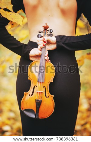 A girl in a dress holds a violin behind her back