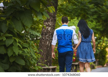 girl in a dress and a man in a shirt and trousers walk in the park in the summer