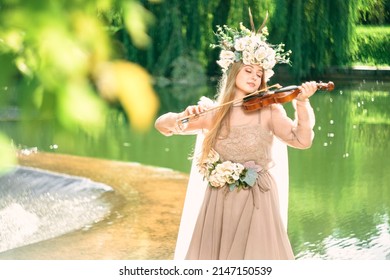 girl in a dress plays the violin near a waterfall
