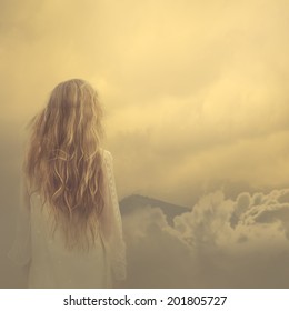 girl in a dress stands in the clouds over the mountains