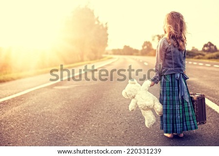 The girl in a dress with a suitcase looking at the sun