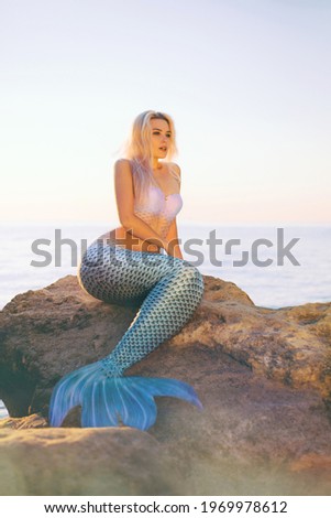 A girl dressed as a mermaid is resting on the rocks