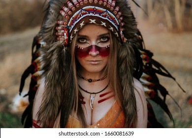 A girl dressed as a Native American with roach and streaks of red paint on the body looking at the camera - Shutterstock ID 1660081639