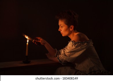 Girl Dressed In Peasant Dress Heats Knife Blade Over A Candle Flame