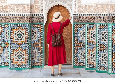 Girl dressing in red with hat looking the Ben Youssef Madrasa in marrakesh, morocco	