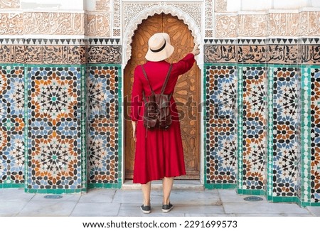 Girl dressing in red with hat looking the Ben Youssef Madrasa in marrakesh, morocco	