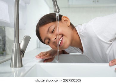Girl drinking tap water over sink in kitchen