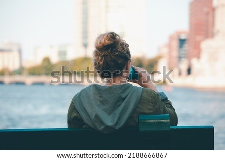 A girl drinking water from bottle while sitting relaxing at Charles River in Boston, USA.