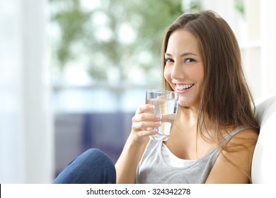 Girl drinking water sitting on a couch at home and looking at camera - Shutterstock ID 324342278