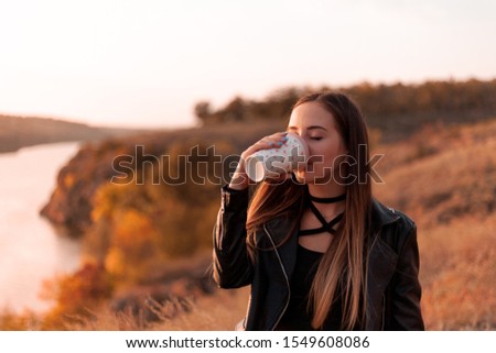 Girl drinks coffee on the nature. Autumn day, sunset.