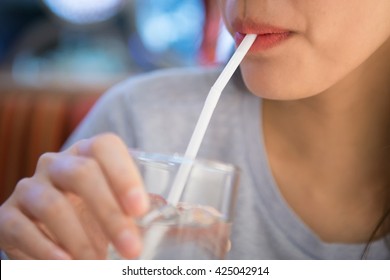 The girl drinks water from a glass through a straw