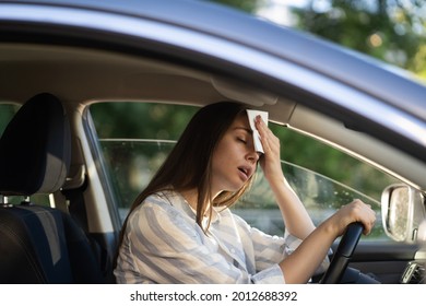 Girl driver being hot during heat wave in car, suffering from hot weather, has problem with a non-working air conditioner, wipes sweat from her forehead with tissue. Summer, heat concept. 