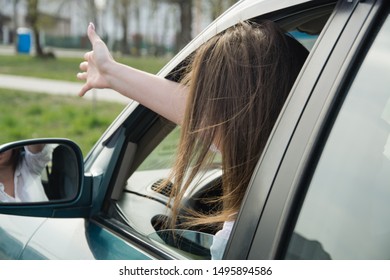 A girl drives a car and swears, shows her hand through the window to another driver or pedestrian. Woman driving.