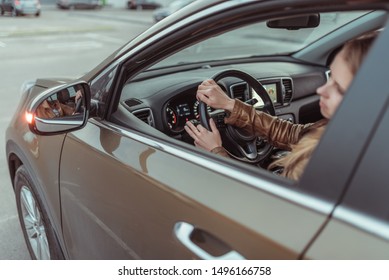 A girl driving a car, looks in a side view mirror, parking at shopping center, turning at an intersection, turning on a turn signal on a car. Left turn. Woman in a leather jacket.