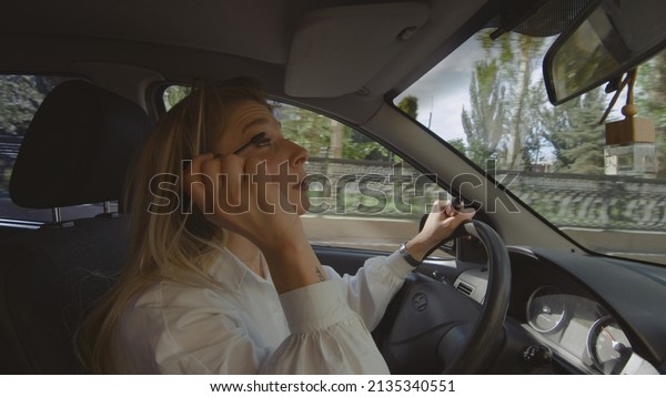 A girl driving a car\
paints her eyelashes with mascara. People are driving in a car.\
Traffic rules