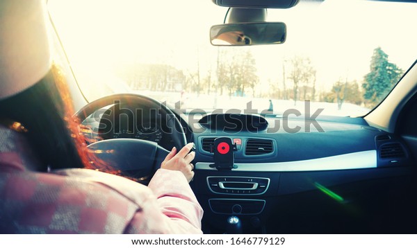 Girl driving the car rear\
view. The bright sun blinds the eyes of the driver. Driving in\
winter.