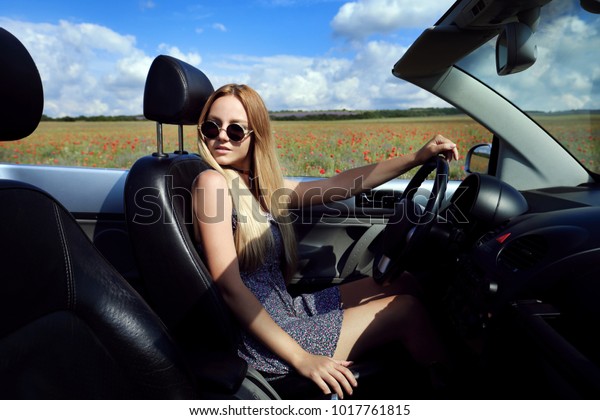 Girl\
driving a convertible car in a summer poppy\
field