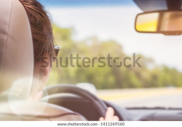 The girl\
is driving on the highway in Spain. View from the back seat of the\
car on the windshield, road and the\
driver