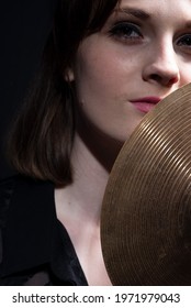 Girl Drummer Holding A Small Drum Cymbal In Her Hands. Dramatic Portrait On Black Background