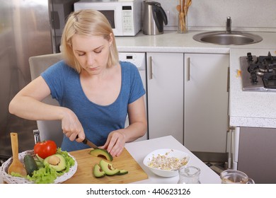 Girl Eating An Avocado And Salad, Healthy Eating, Diet. Pensive Woman Looks At The Tomato. In The Kitchen. Bright Room