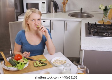 Girl Eating An Avocado And Salad, Healthy Eating, Diet. Pensive Woman Looks At The Tomato. In The Kitchen. Bright Room