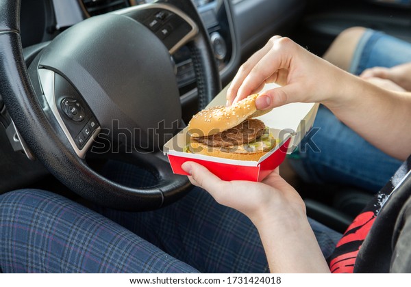 Girl eating a burger sitting in a car. Fast\
food, takeaway, snacks on the\
road.