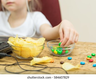 Girl Eating Candy And Potato Chips Of The Laptop. Unhealthy Eating Child At The Computer.