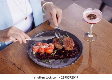 Girl Eating Meat Medallion With Tomatoes Close-up In A Modern Restaurant