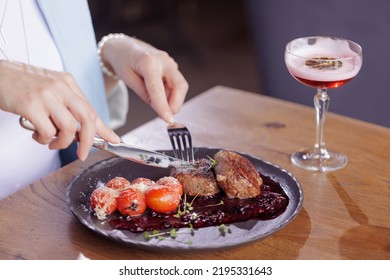 Girl Eating Meat Medallion With Tomatoes Close-up In A Modern Restaurant