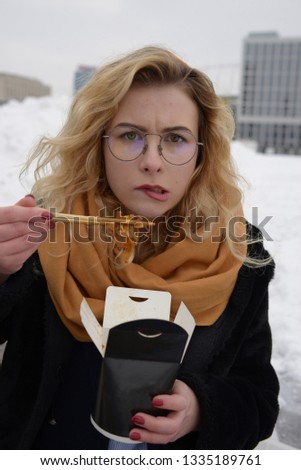 Girl eating noodles out of the box. Bright blond woman eating asian fast food from takeaway box with chopsticks.