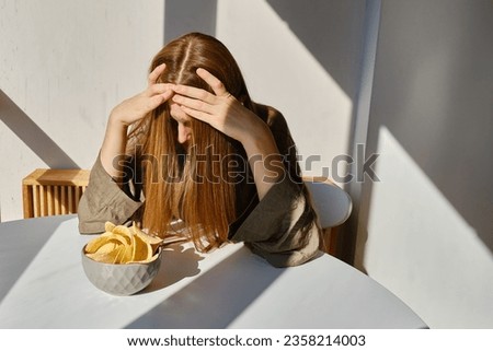 A girl eats crispy potato chips from a bowl on the couch. Quick snack. Calories and diet
