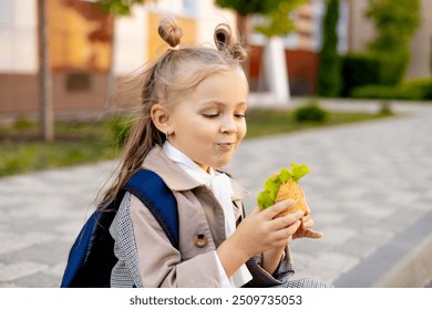 a girl eats her lunch at school, a schoolgirl eats a sandwich or burger in the school yard, a snack or a child's lunch. - Powered by Shutterstock