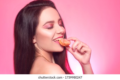 Girl eats macaroon, model on a pink background eats a sweet, sugar diet. Brunette with pink make-up, addicted to food. Macaroon bites, cookies - Powered by Shutterstock