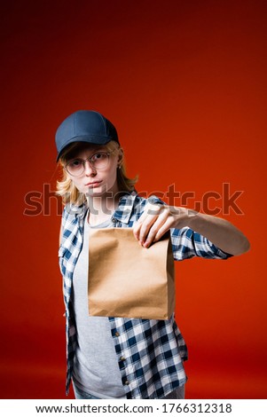 Girl employee network of fast food restaurants in the shirt and cap holding a cooked order food in a paper bag