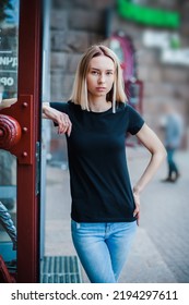 A Girl In An Empty Black T-shirt Stands Leaning Against The Open Door. Mockup For T-shirt Print Shop