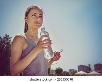 Girl is engaged in sports while listening to music. She is resting and drinking water.