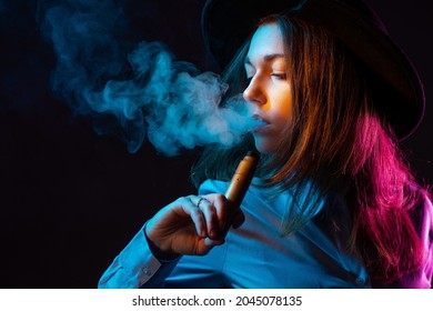 Girl is engaged in vaping. Young vaper woman on black background. Concept - vape shop. Sale of devices for vaping. Vaper blows smoke from his mouth. Buying e-cig in vape shop. Electronic cigarettes.