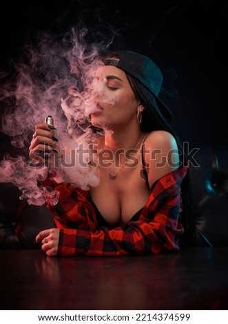        Girl is engaged in vaping. Young vaper woman on black background. Concept - vape shop. Sale of devices for vaping. Vaper blows smoke from his mouth. Buying e-cig in vape shop. Electronic cigare