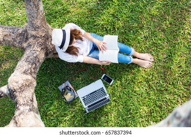 Girl enjoy listening music and reading a book and play laptop on the grass field of the park in the morning (greenery tone),Woman using tablet in park on a sunny day