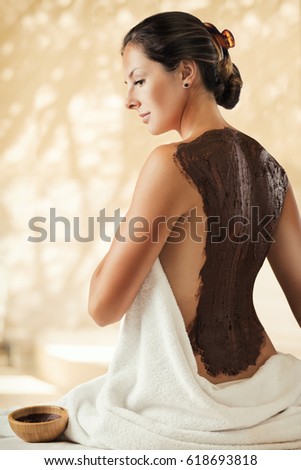 The girl enjoys chocolate body mask in a spa salon.