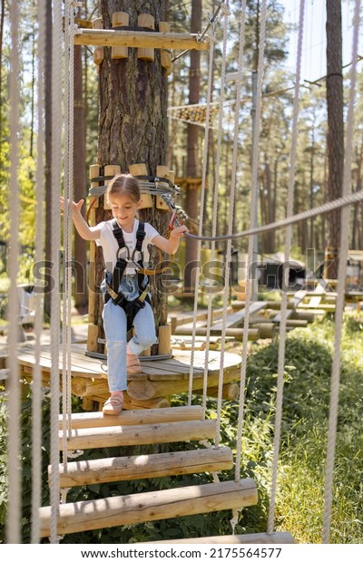girl enjoys climbing in the ropes course
adventure. child engaged climbing high wire park.Toddler climbing
in a rope playground structure.
