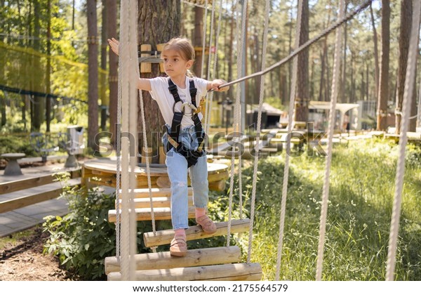girl enjoys climbing in the ropes course\
adventure. child engaged climbing high wire park.Toddler climbing\
in a rope playground structure.\
