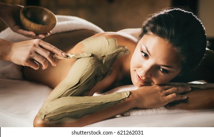 The girl enjoys mud body mask in a spa salon. Focus on the hand with the stick. Luxury treatment. - Powered by Shutterstock