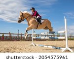 A girl equestrian athlete jumps on a horse high barrier. Athlete in equestrian equipment, protective helmet. Vertical photo. Children