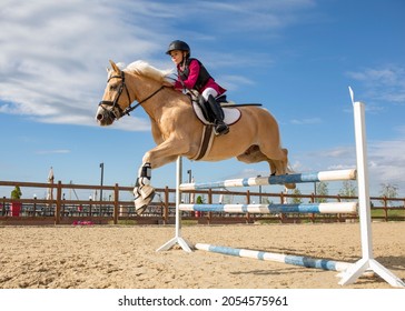 A girl equestrian athlete jumps on a horse high barrier. Athlete in equestrian equipment, protective helmet. Vertical photo. Children's sports. Image with selective focus and noise effect, toning